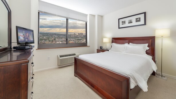 A hotel room with a large bed, a desk with a flat-screen TV, a window with a city view, and a framed picture on the wall.