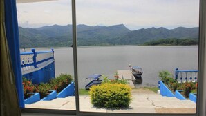 A view from a window overlooking a lake with mountains in the background, a dock with a boat, and blue railings. - Marineros Club Nautico (Prado)