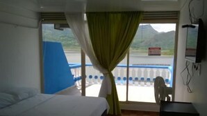 A hotel room with a bed, a desk, and a view of a mountainous landscape through the window. - Marineros Club Nautico (Prado)