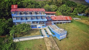 A multi-story building with a blue and red exterior, surrounded by lush greenery and hills. - Marineros Club Nautico (Prado)