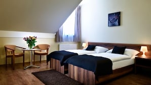 A hotel room with two beds, a small table with chairs, a vase of flowers, and a painting on the wall. - Hotel Rozálka (Pezinok)