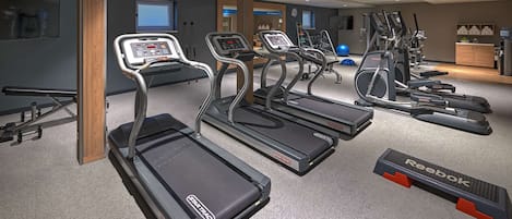 A gym with treadmills, ellipticals, and a Reebok step platform.