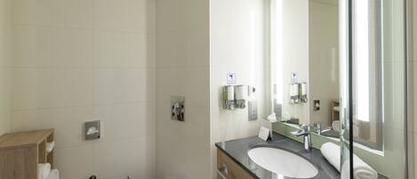Un baño moderno con cabina de ducha de vidrio, inodoro blanco, tocador con lavabo y un espejo grande.
