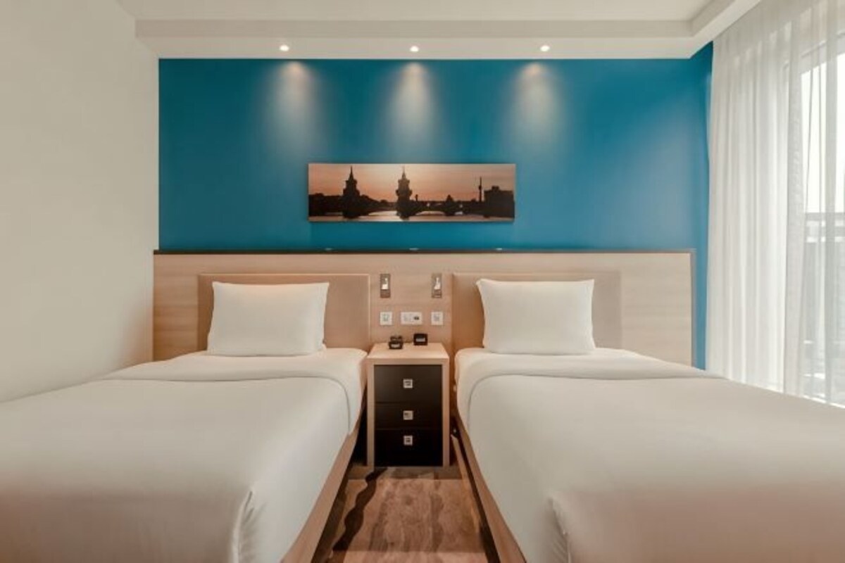 A hotel room with two beds, a nightstand, and a wall-mounted painting.