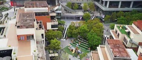A multi-story building with a rooftop garden, a covered outdoor area with seating, and a visible water feature.