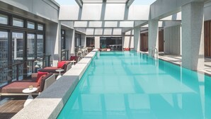 A modern indoor swimming pool with a glass ceiling, red and white seating, and a view of the cityscape. - Cordis Shanghai Hongqiao (Shanghai)
