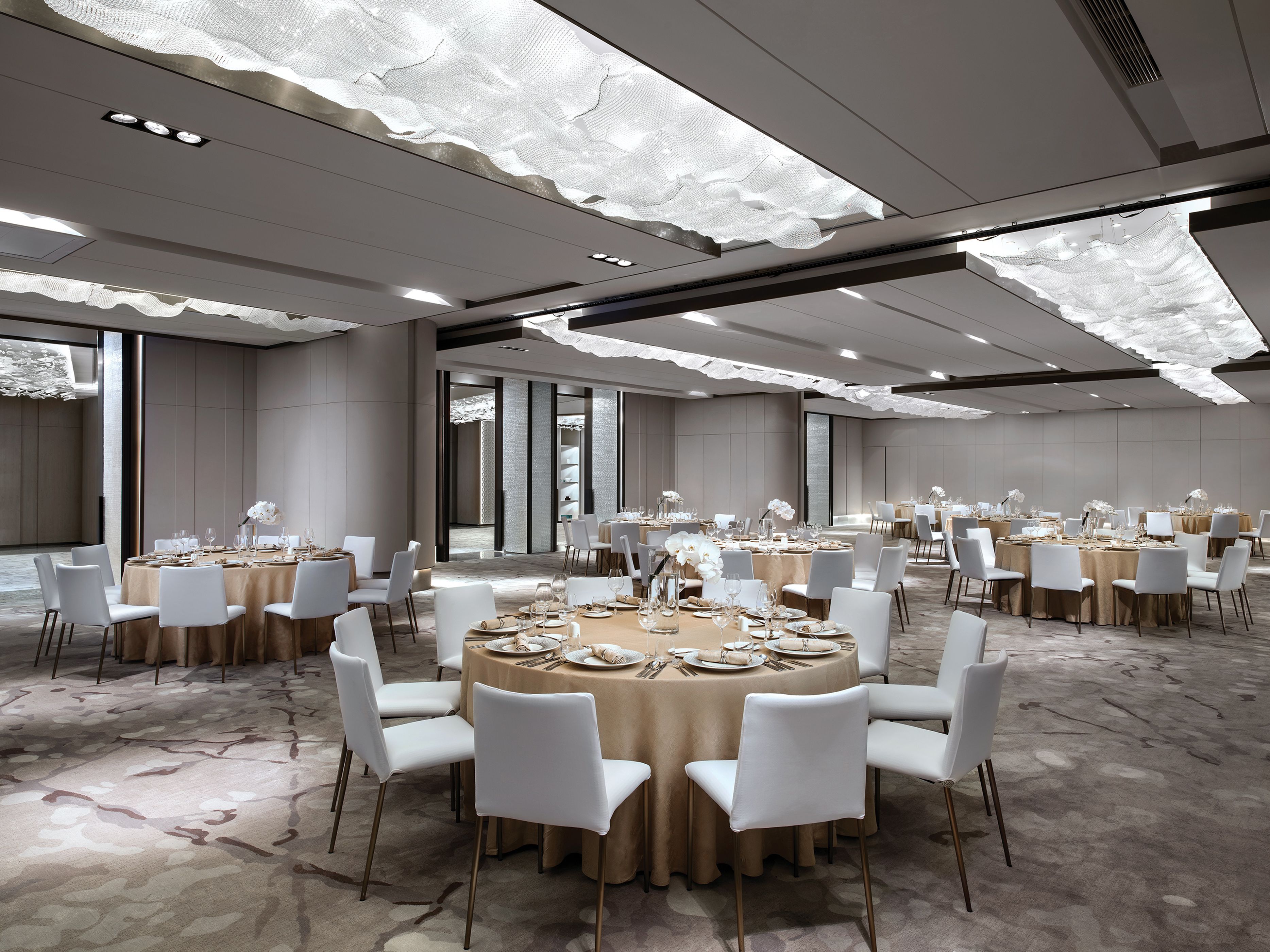 Un'ampia sala conferenze con tavoli rotondi, sedie bianche e un moderno design del soffitto.