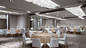 Un'ampia sala conferenze con tavoli rotondi, sedie bianche e un moderno design del soffitto.