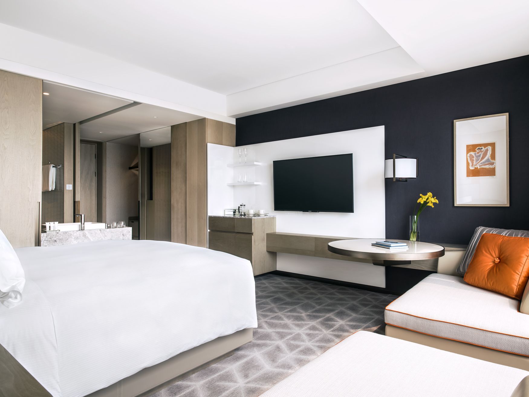 A modern hotel room with a large bed, a sofa, a TV, and a small table with a vase of flowers.