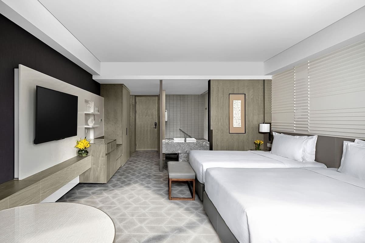 Habitación de hotel moderna con una cama grande, un televisor de pantalla plana, un escritorio y un baño visible a través de una puerta abierta.