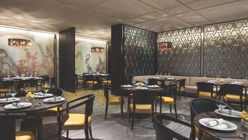 Un interior de restaurante moderno con varias mesas y sillas, paneles decorativos en las paredes e iluminación ambiental.