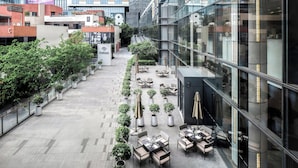 A modern building with a glass facade, outdoor seating area with tables and chairs, and potted plants. - Cordis Shanghai Hongqiao (Shanghai)