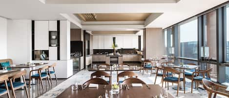 Un espace de restauration moderne dans un hôtel, avec une grande table centrale dressée pour un repas, entourée de chaises.
