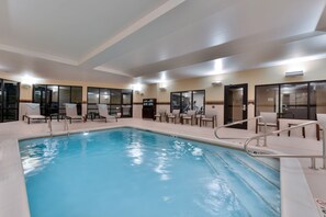 An indoor swimming pool with clear water, surrounded by lounge chairs and a tiled floor.