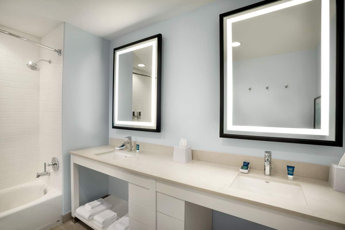 A modern bathroom with two sinks, a bathtub, and a large mirror.