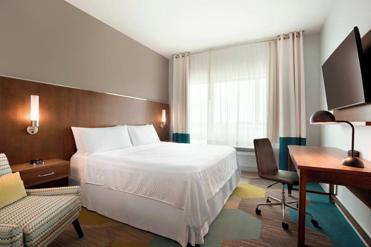 A hotel room with a bed, a desk, a chair, a TV, and a lamp.