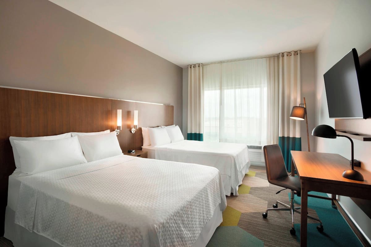 A hotel room with two beds, a desk, a chair, a TV, and a window with curtains.