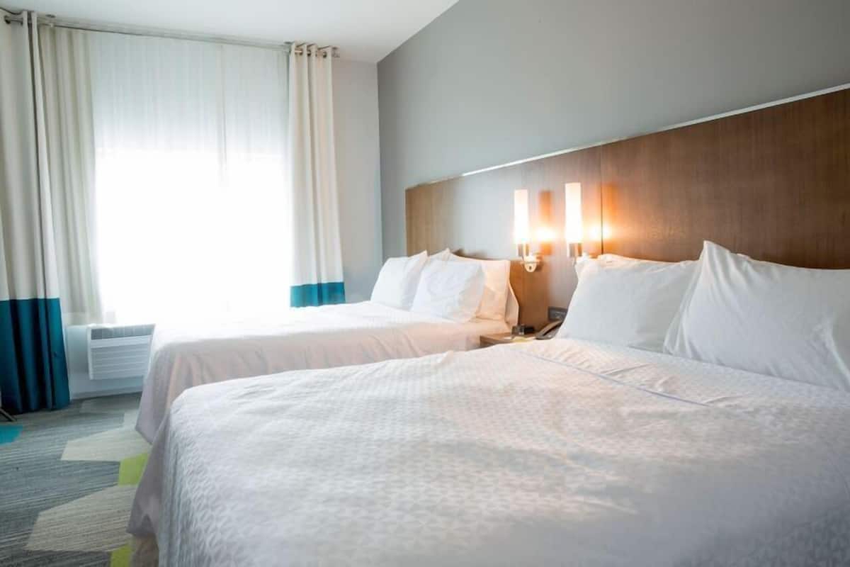 A hotel room with two beds, a wooden headboard, bedside lamps, and a window with curtains.