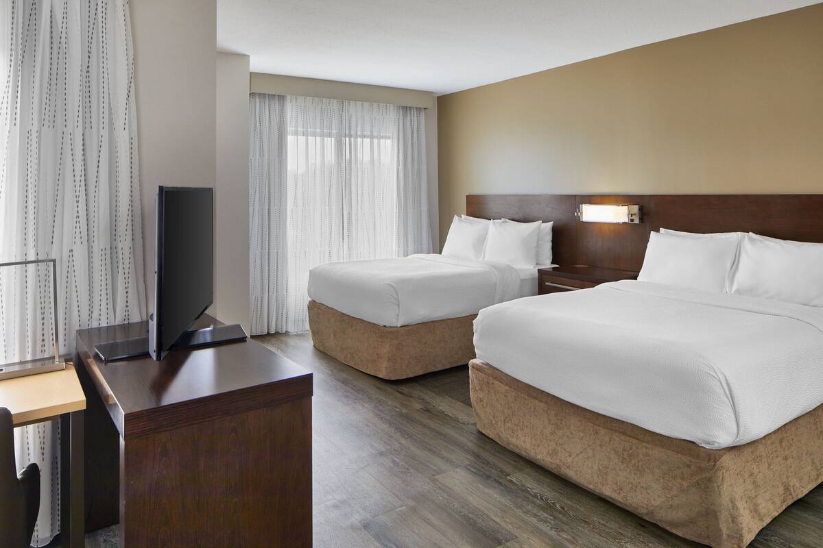 A hotel room with two beds, a desk, and a TV.