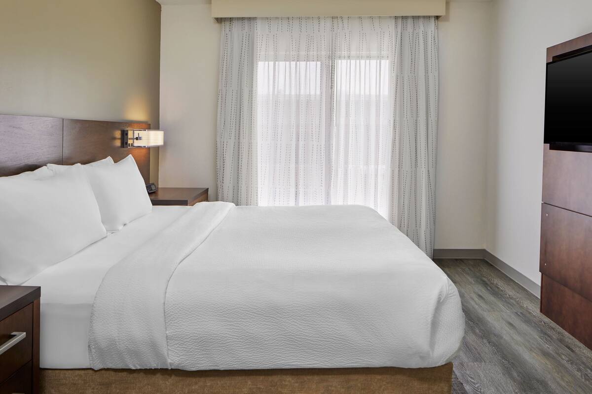 A hotel room with a large bed, a nightstand with a lamp, a TV, and a wooden wardrobe.