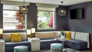 Ein modernes Wohnzimmer mit einem Ecksofa, Hocker, einem Couchtisch und einem an der Wand montierten Fernseher.