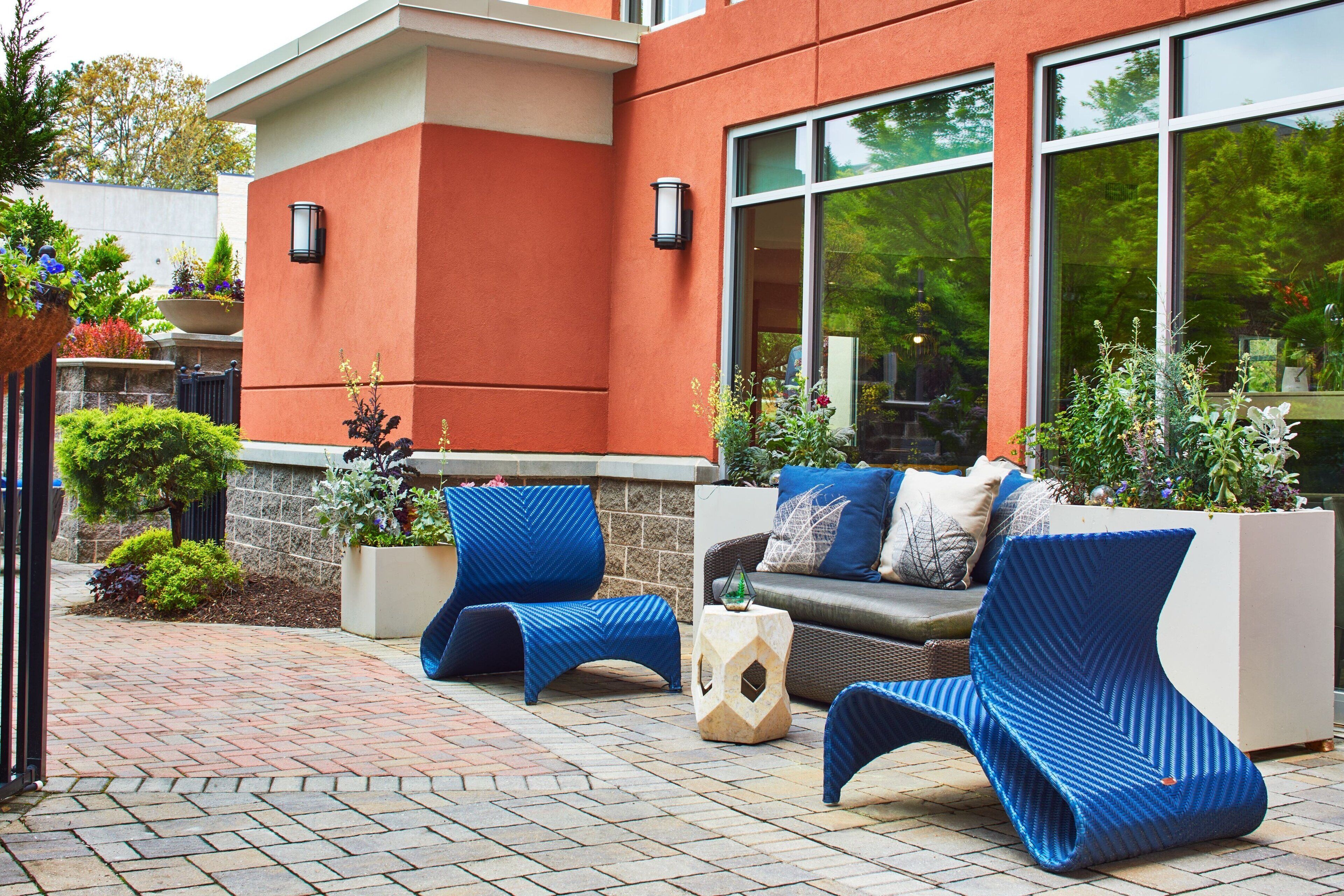 An outdoor seating area with modern blue chairs and a sofa, surrounded by potted plants and a stone pathway.