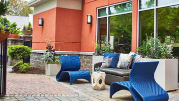 An outdoor seating area with modern blue chairs and a sofa, surrounded by potted plants and a stone pathway.