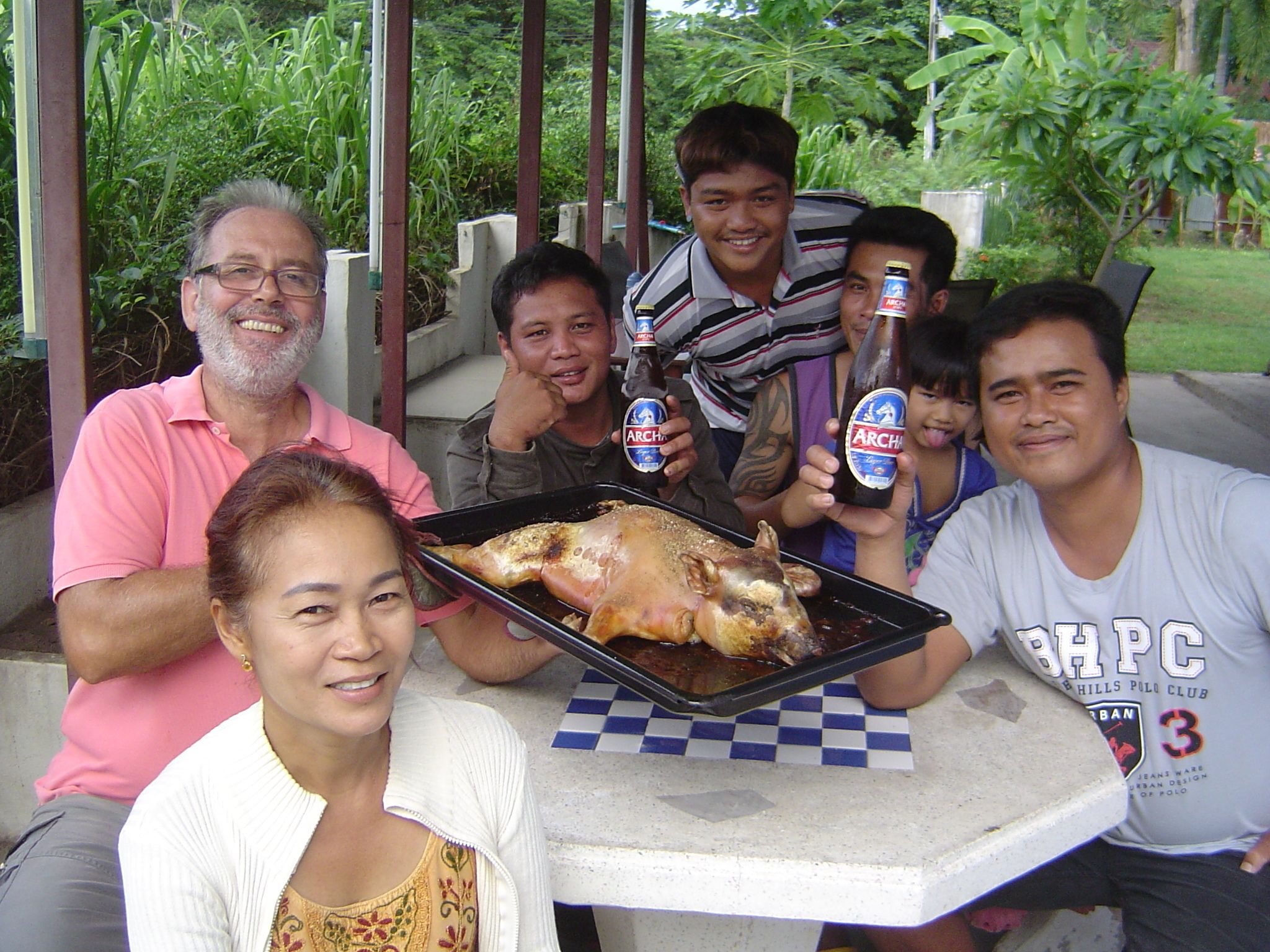 A group of people sitting at a table with roasted chicken and beer bottles.