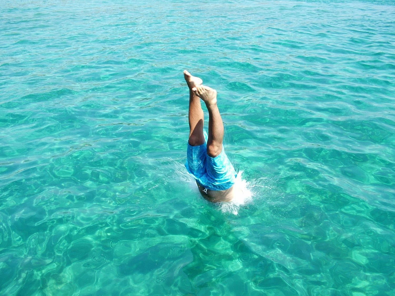 A person performing a handstand in clear blue water.