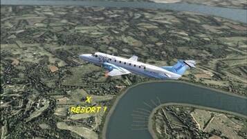 Un jet privado volando sobre una zona turística con una masa de agua y una carretera curva.