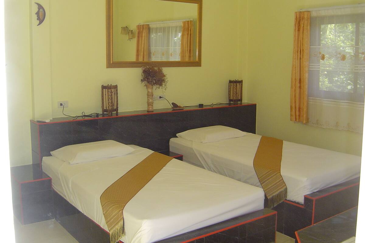 A hotel room with two single beds, a bedside table with a vase, a mirror, and a window with curtains.