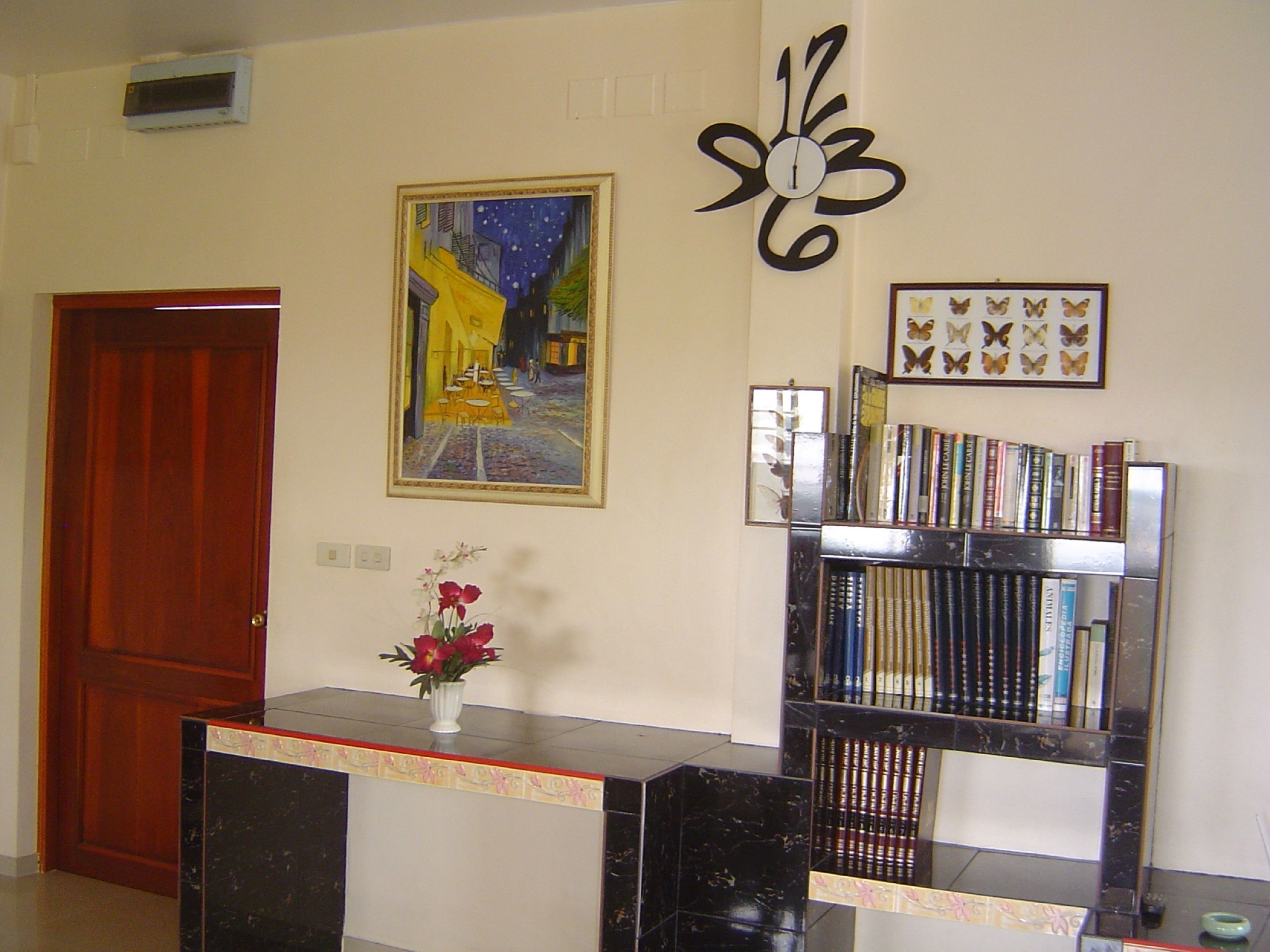 A reception area with a marble counter, a painting of a street scene, a decorative clock, and a bookshelf with books.