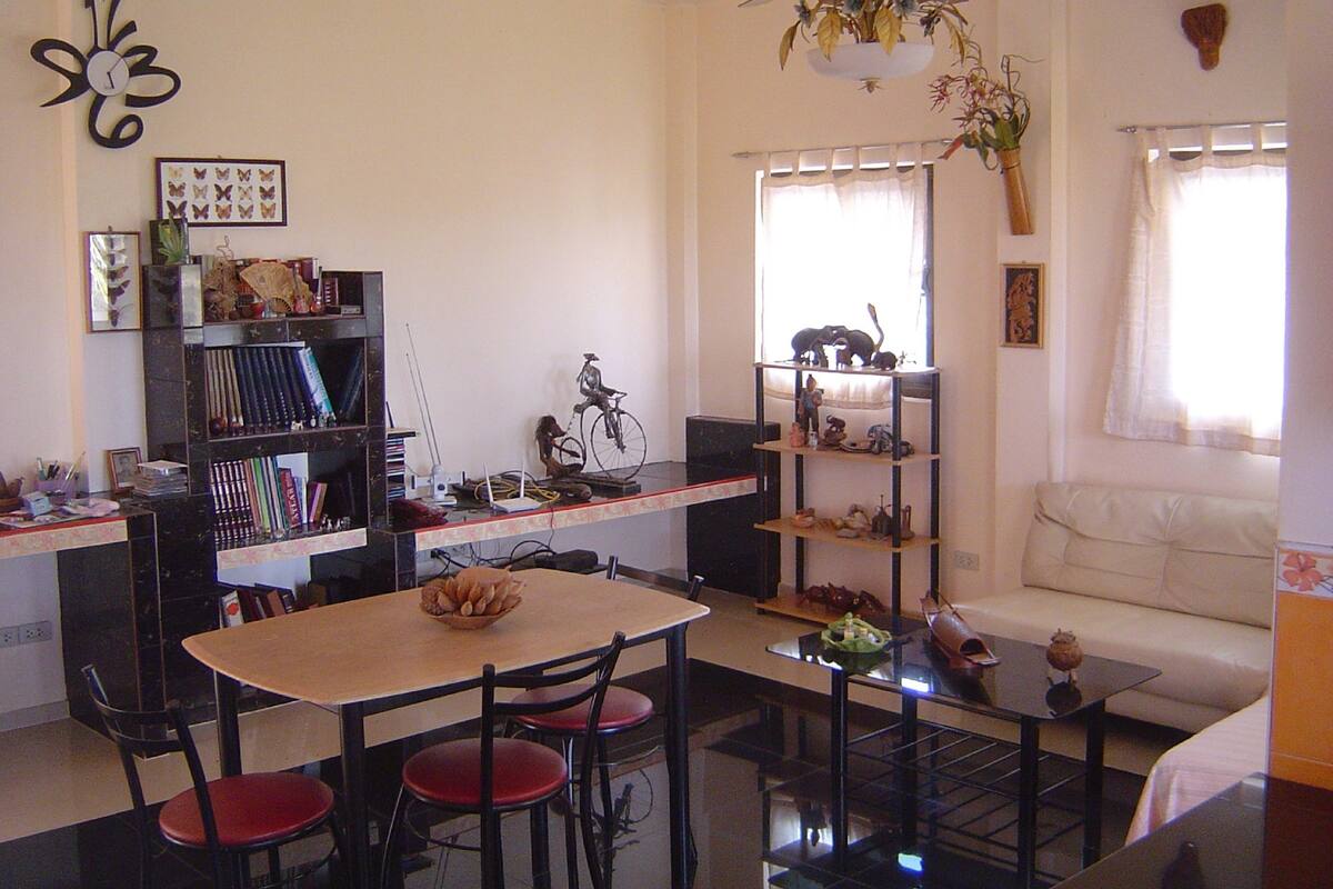 A living room with a dining table, chairs, a bookshelf, a sofa, and a ceiling fan.