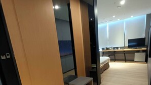 Una habitación de hotel moderna con piso de madera, un escritorio con una silla, un televisor y un pequeño rincón de descanso.