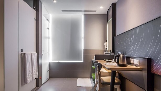 Habitación de hotel moderna con diseño minimalista, que incluye un espejo grande, un escritorio con hervidor de agua y vistas a la ciudad a través de la ventana.