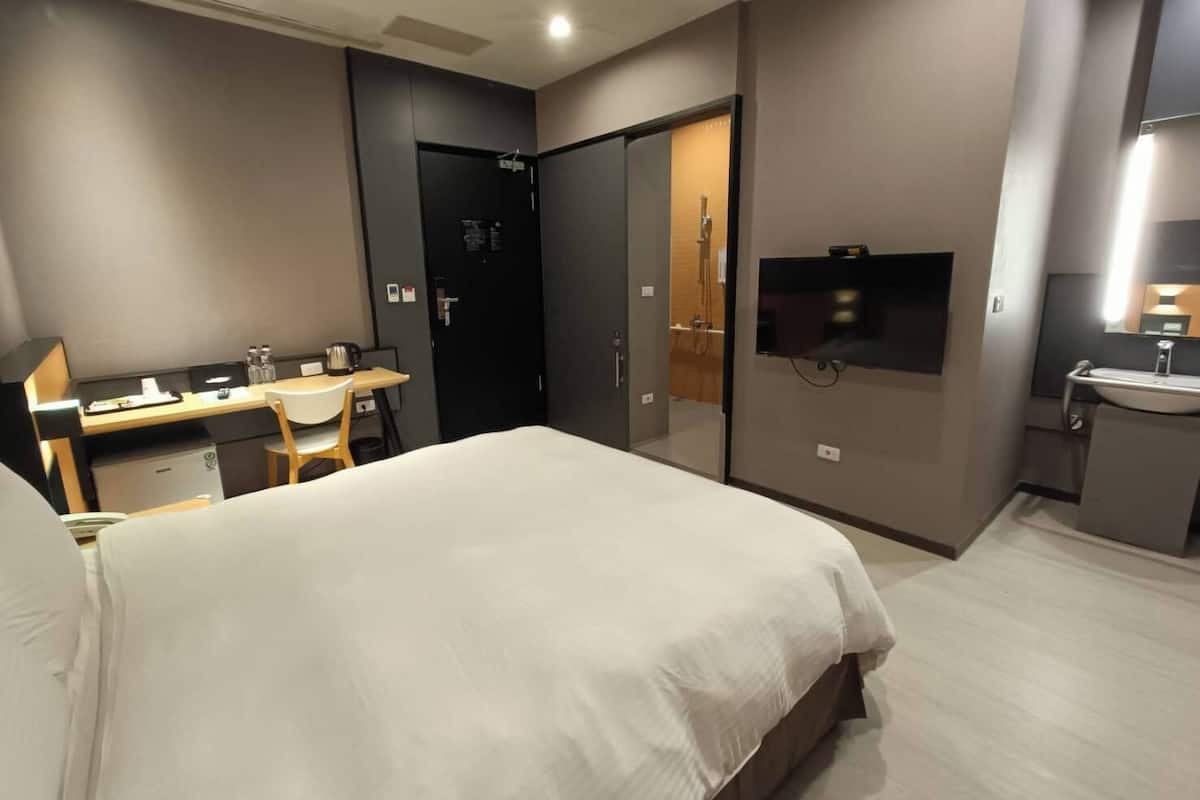 Quarto de hotel moderno com uma cama grande, uma mesa com cadeira, uma televisão e um banheiro com pia e espelho.