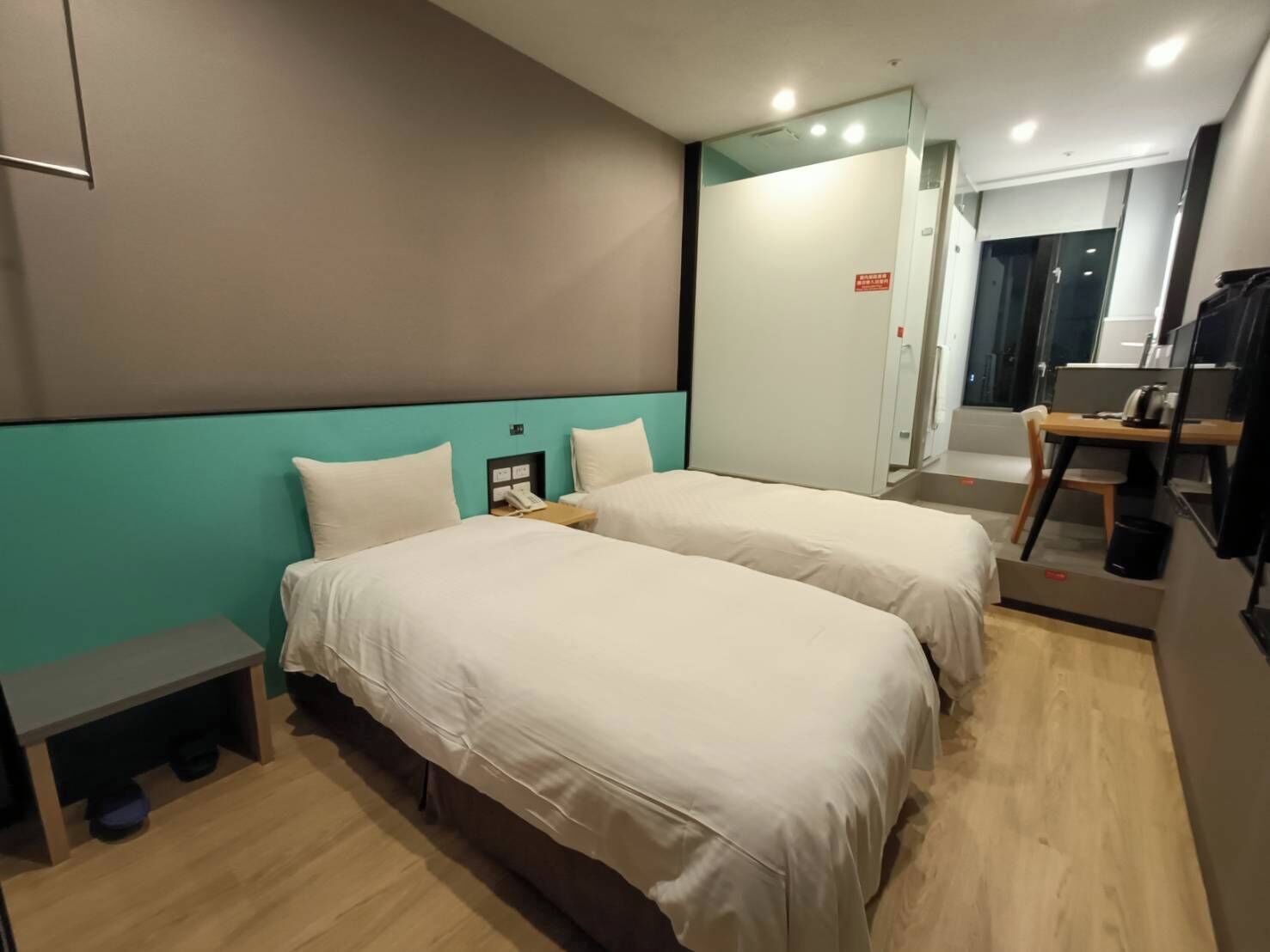 A hotel room with two beds, a small desk, a mirror, and a view of the hallway.