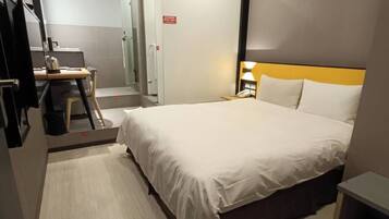 A modern hotel room with a large bed, a desk with a chair, a mirror, and a shower area.