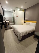 Una habitación de hotel moderna con una cama grande, un escritorio con silla, un espejo y zona de ducha.