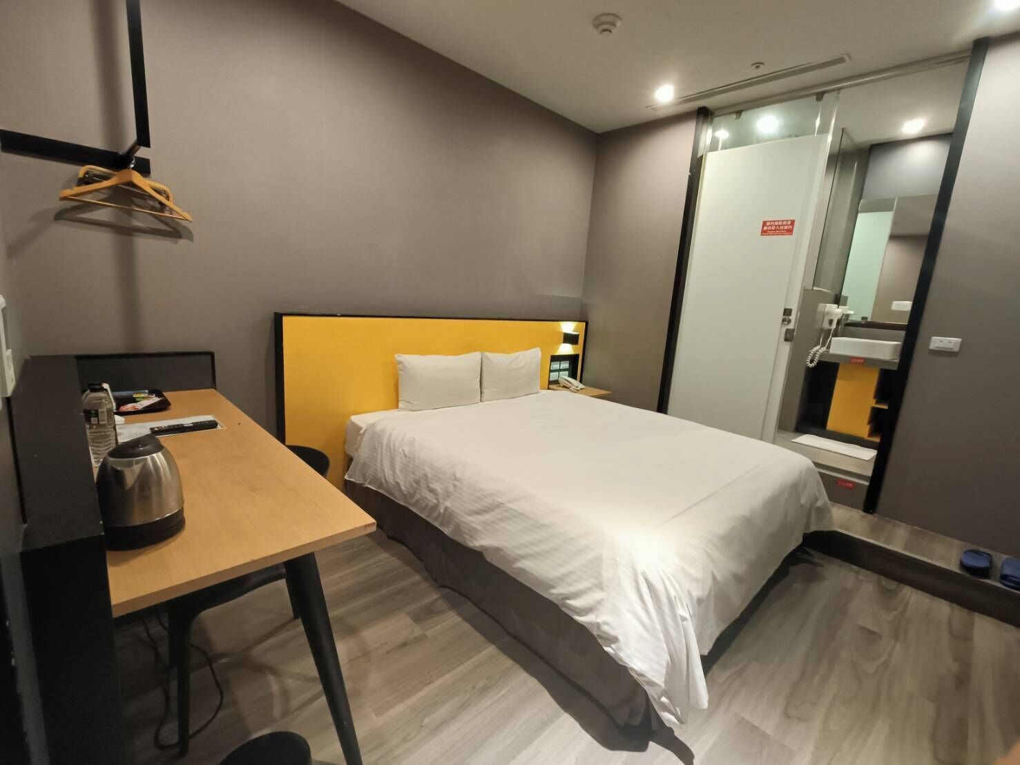 A hotel room with a bed, a desk, a kettle, and a mirror.
