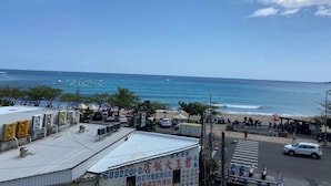 Blick auf die Küste mit Strand, einem 7-Eleven Geschäft und einem Gebäude mit einer Schrifttafel in einer Fremdsprache.