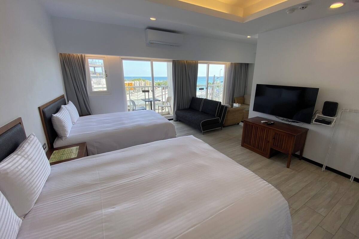 A hotel room with two beds, a TV, and a balcony with a view of the city.