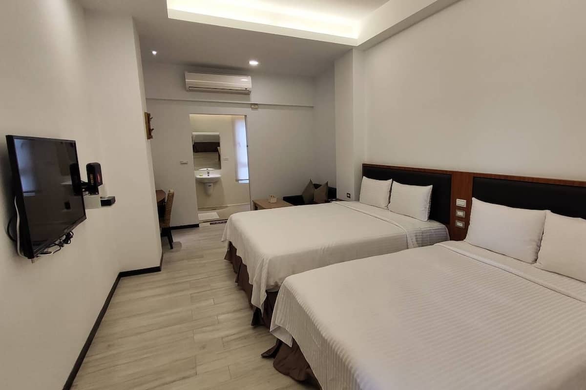 A hotel room with two beds, a TV, and an air conditioning unit.