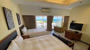 Ein Hotelzimmer mit zwei Betten, einem Fernseher und einem Balkon mit Meerblick.