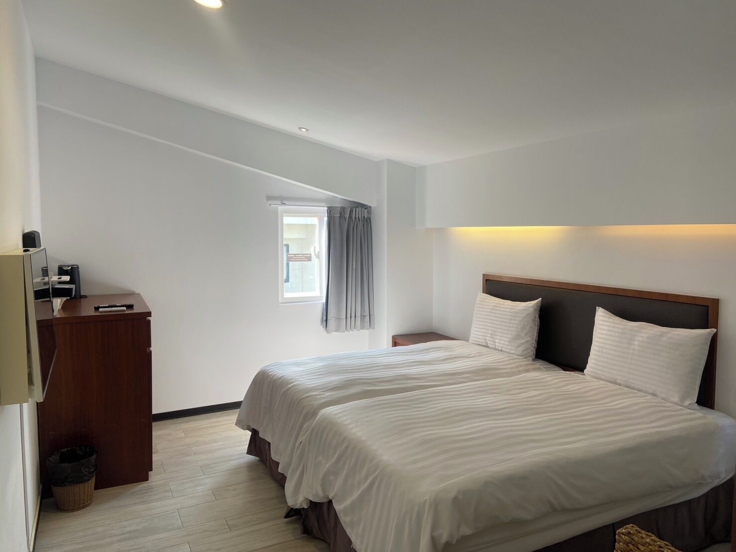 A hotel room with a large bed, a desk, and a small window with curtains.