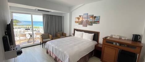 A hotel room with a large bed, a desk, a chair, a TV, and a view of the ocean.