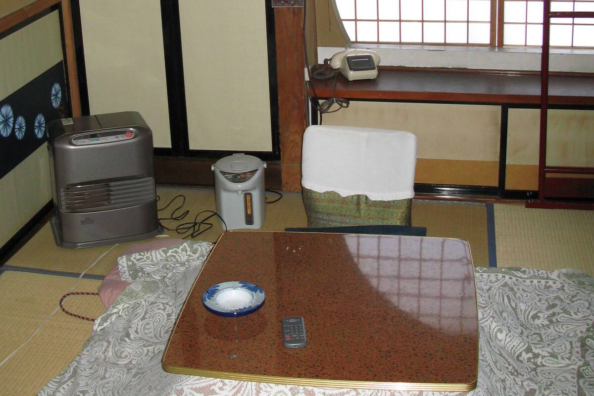 A traditional Japanese room with tatami flooring, a low table with a blue dish, a remote control, and a heater.