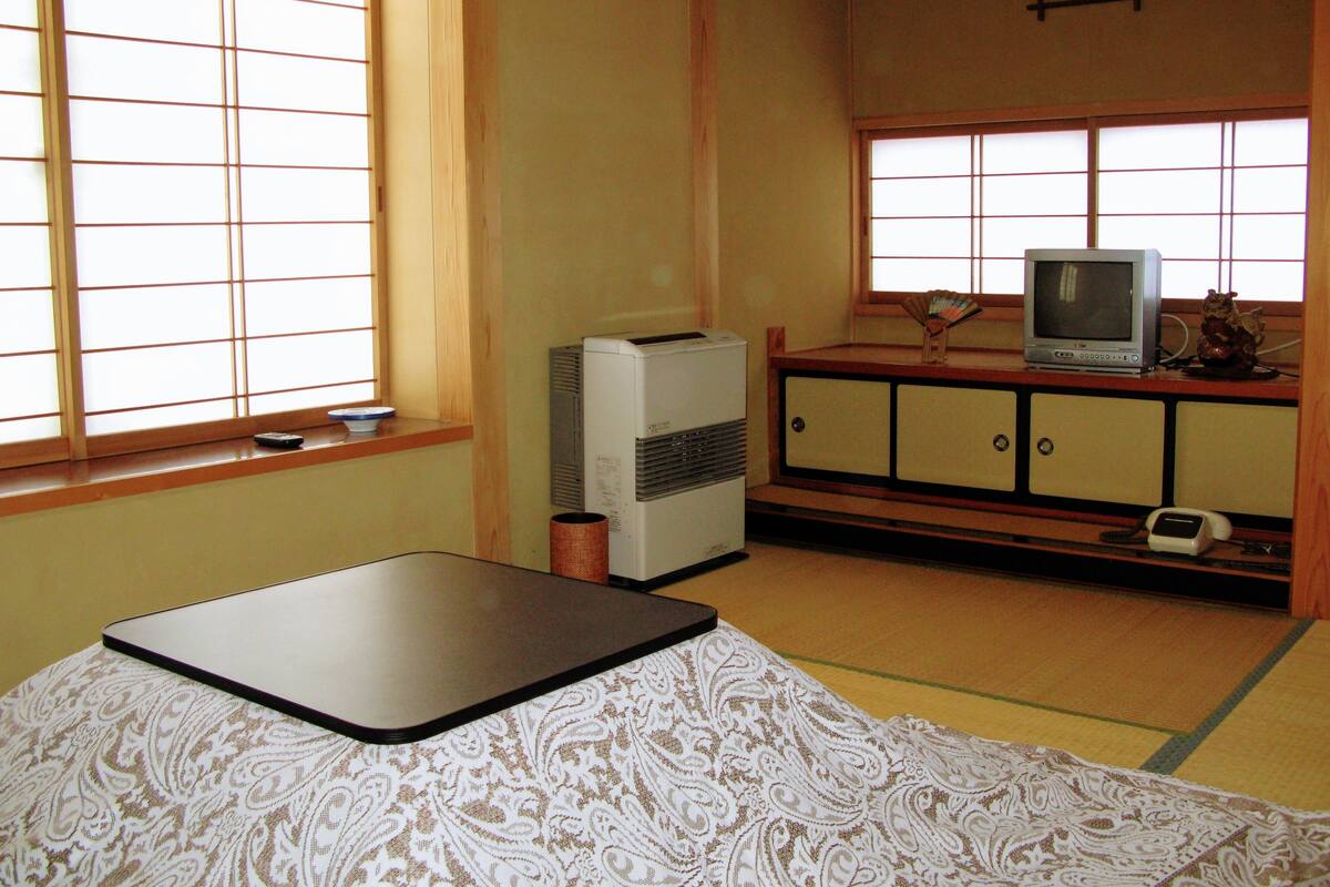 A traditional Japanese room with tatami flooring, a low table, a television, and a small cabinet.
