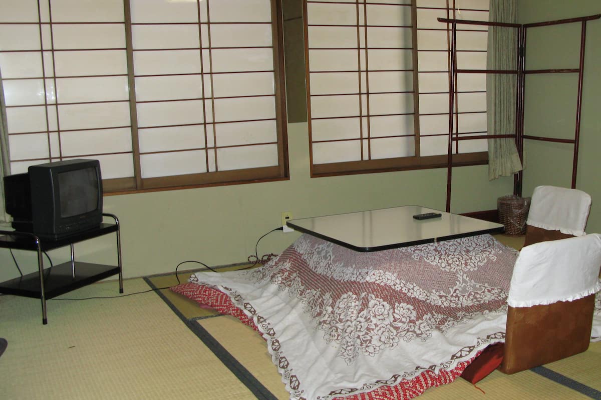 A traditional Japanese room with tatami flooring, a low table, a television on a stand, and a shoji screen.