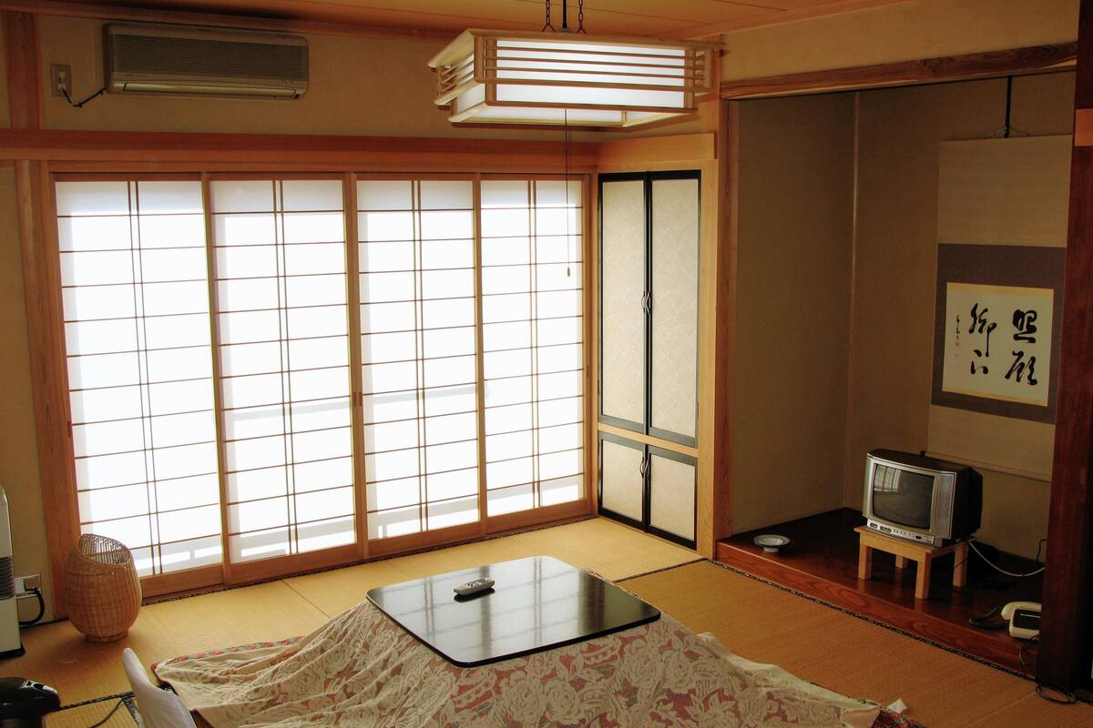 A traditional Japanese room with tatami flooring, a tatami mat table, a television, and sliding doors.